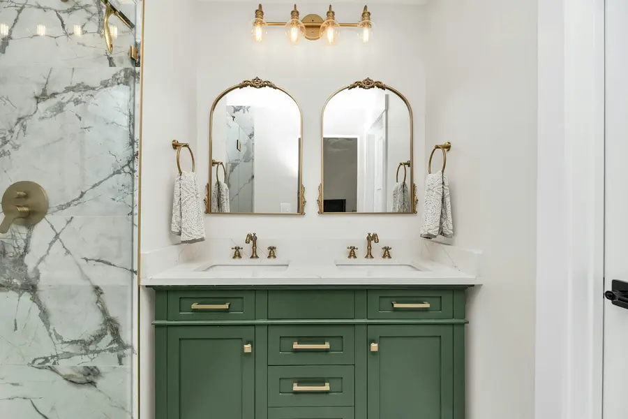 Bathroom remodel with a green shaker vanity and marble-tiled shower