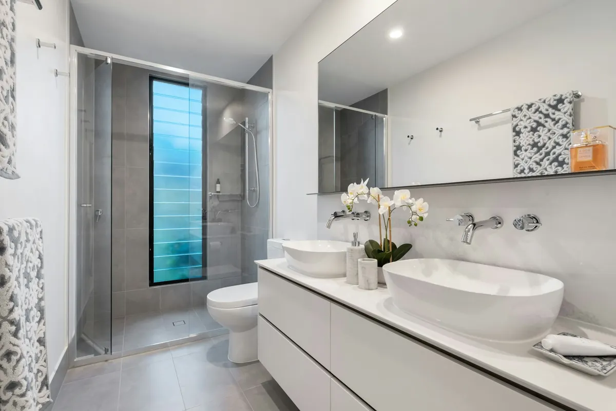 Gray-and-white bathroom with a glass shower and twin vessel sinks